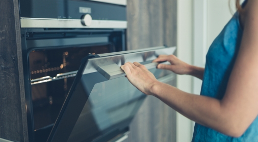 A young woman is opening the oven in her modern kitchen