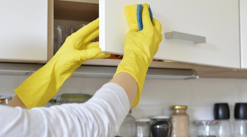 woman in yellow gloves washes the door in kitchen cabinet