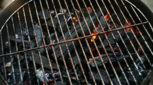 A close-up of a rusty old barbeque grill with burning charcoal underneath it.