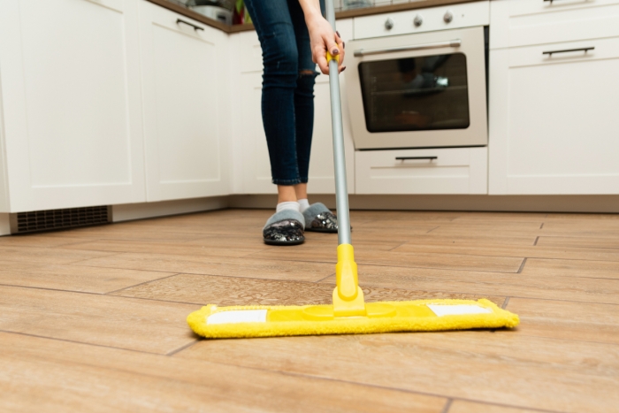 woman washes wooden floors from a laminate floor in a bright kitchen.