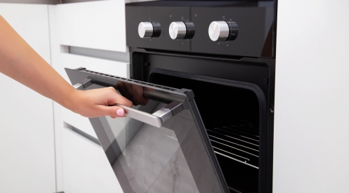 A woman's hand opens the door of an electric convection oven. Built-in oven in the kitchen, energy consumption