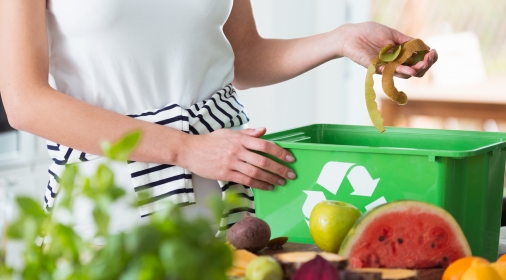 Woman recycling organic kitchen waste by composting in green container during preparation of meal