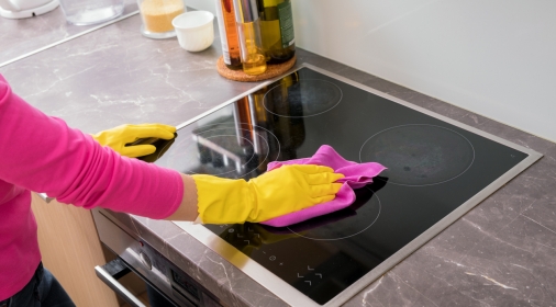 Lady with yellow gloves cleaning an electric glass stove hob