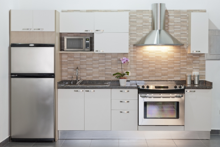 Small or compact modern kitchen with appliances. Contemporary style. Sparse design. White cabinets. Example of design for small architectural spaces. Front view, horizontal composition. Kitchen background.