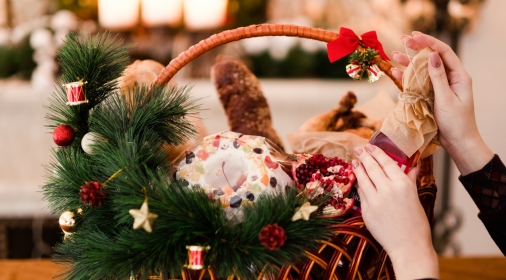 Woman hand arranging Christmas goods in a basket. Festive holiday food gift concept