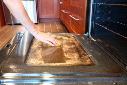 A close up of a person cleaning an oven door with a sponge