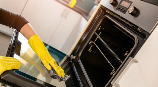 Closeup on woman's hands in yellow protective rubber gloves cleaning oven with rag